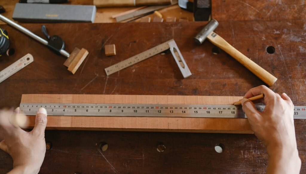 Top view of crop anonymous male using ruler for measuring timber plank on table in workshop